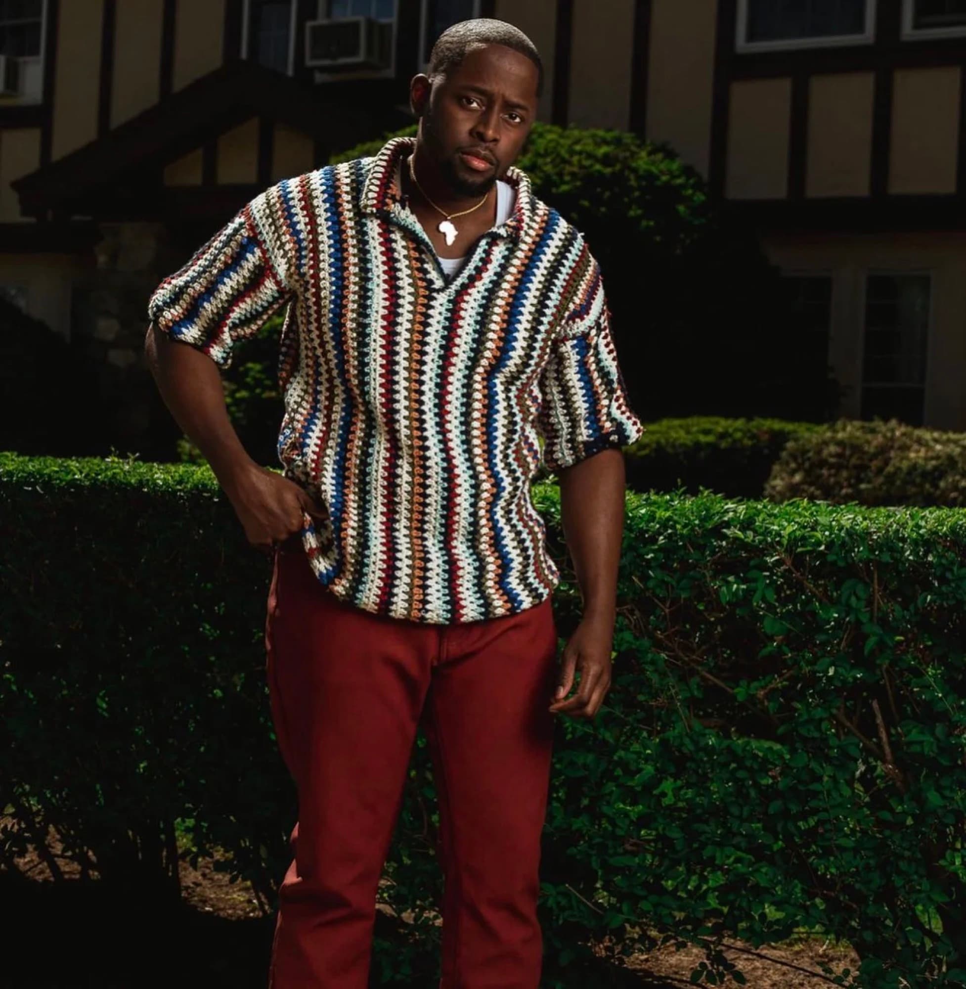 A man wearing a crocheted polo in cream with thin multicolor stripes