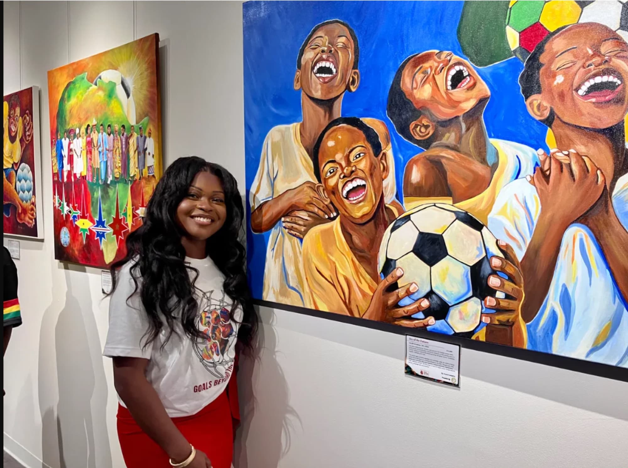 Ivey standing beside her painting of laughing children with a soccer ball at a gallery