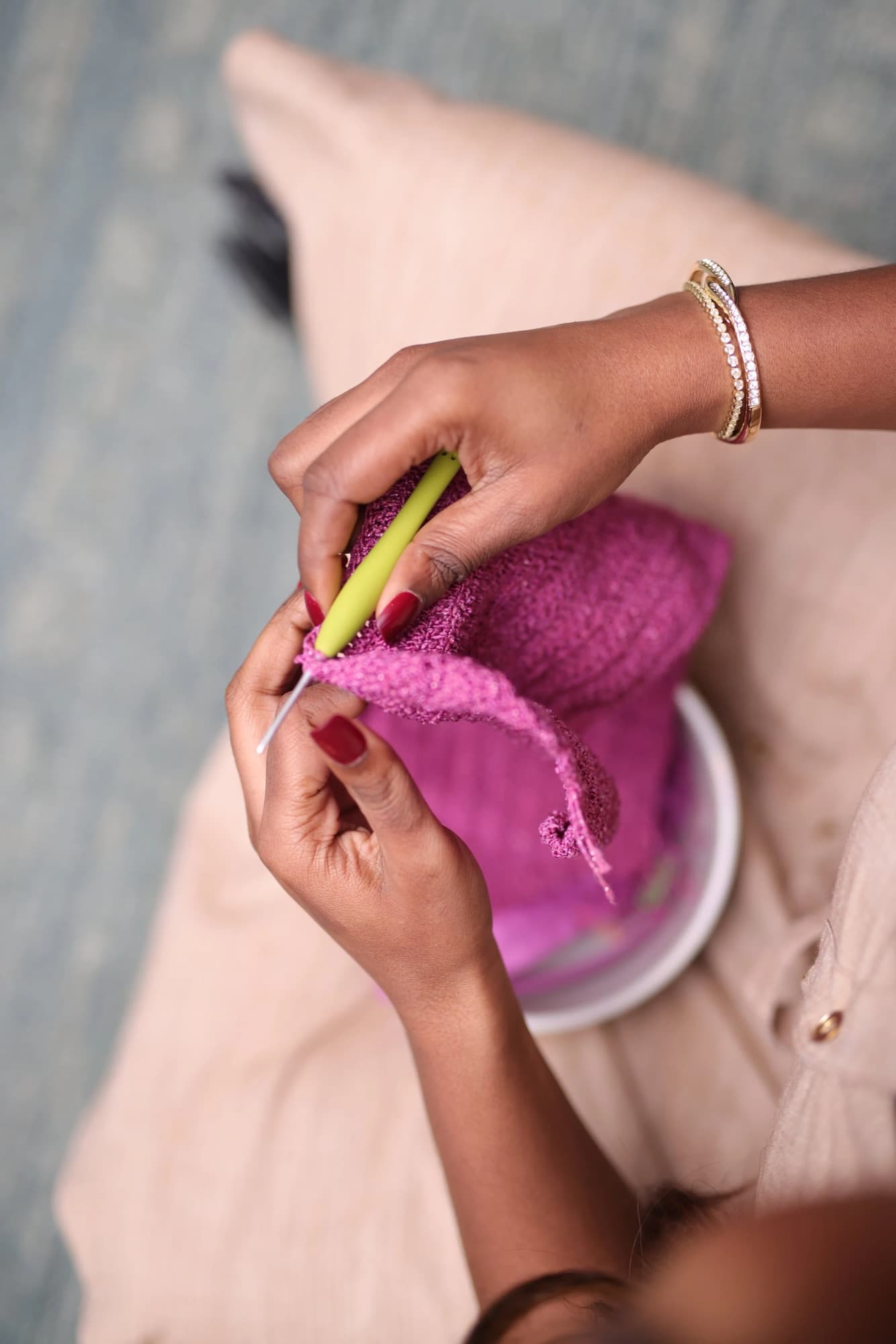 Close-up of hands knitting pink yarn, gold bracelets on the wrist